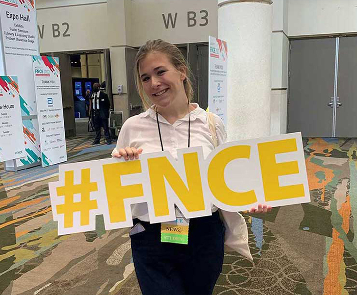 Maddy Baker holding #FNCE letters at conference