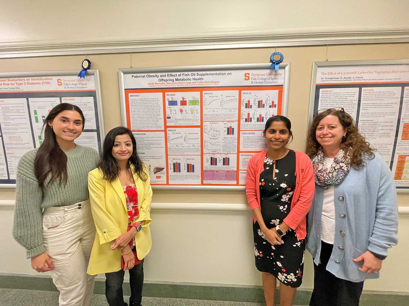 Two students are posed with two professors in front of a research poster