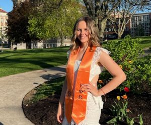 Megan Monzo stands in on campus in graduation regalia