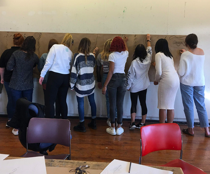 Students in a classroom writing on a large poster board on the wall