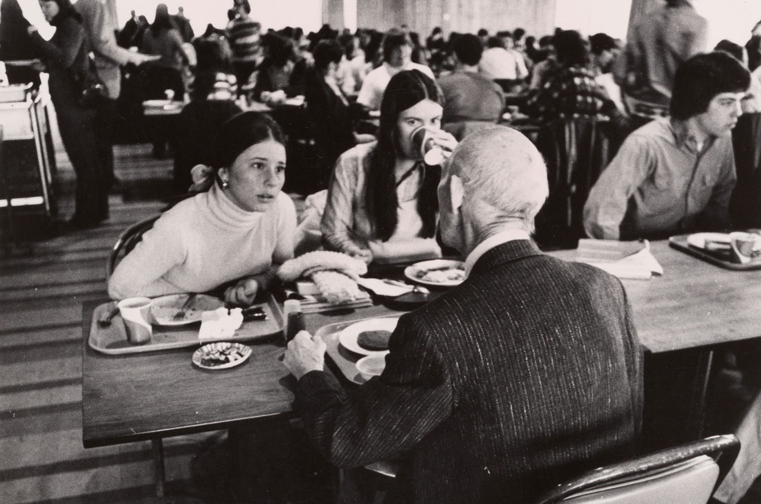 Diane in 1978 sitting at a dining table and talking with a fellow student and professor.