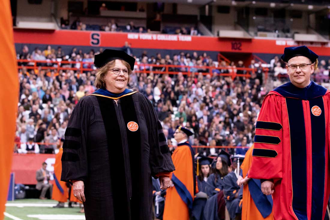 Diane stands in a stadium dressed in regalia.