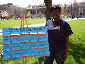 A student stands beside a poster on an easel on the quad