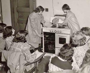 2 women are working over a stove while 6 others look on