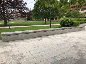 A view of a stone and concrete bench with the quad and trees behind it