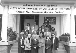 18 adults are standing below a banner which says welcome parents and students to S.U. College of Nursing college that empowers nursing leaders