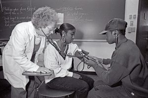 A faculty member works with two nursing students as the one measures the blood pressure of the other