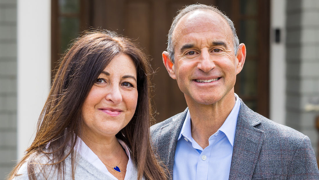 Dina and David Nass are posed together outside in front of a building.