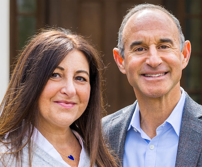 Dina and David Nass are posed together outside in front of a building.