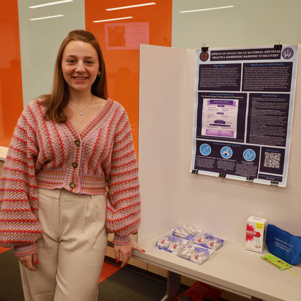 A young women stands next to a research poster