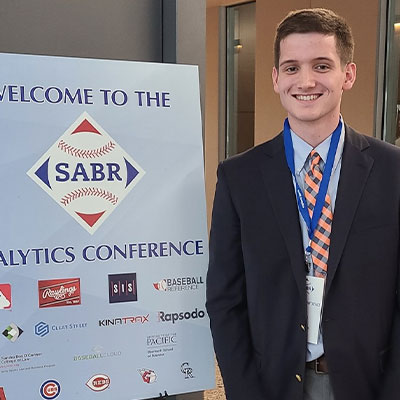 Alex Oppel stands next to a S.A.B.R. Conference sign.