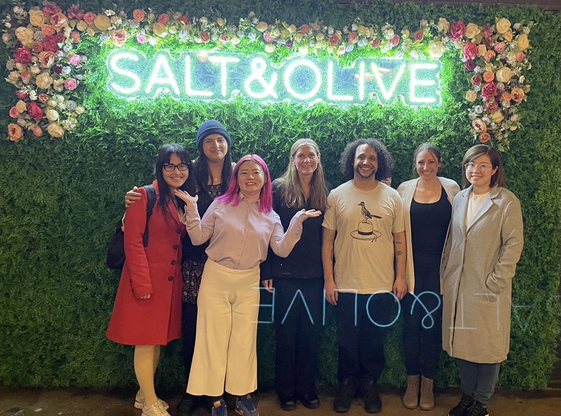 3 students are posed with 4 professors under a lit sign saying Salt and Olive