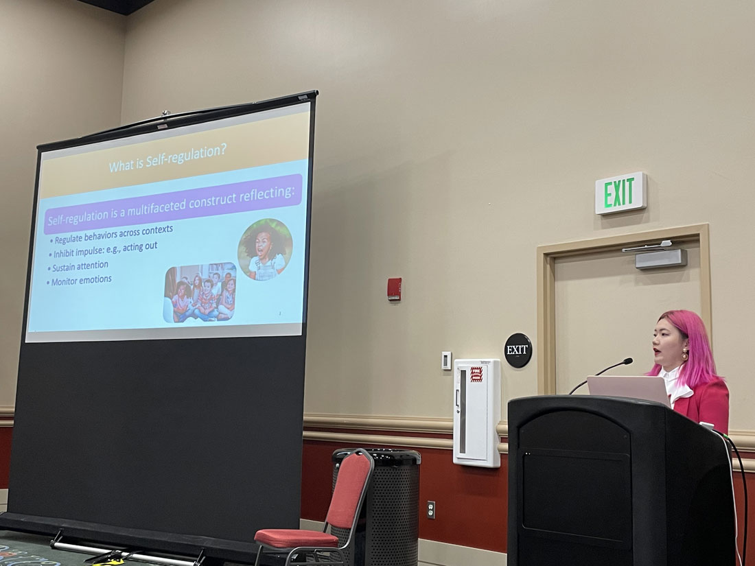 Qingyang presents at a podium with a slide presentation showing in the background