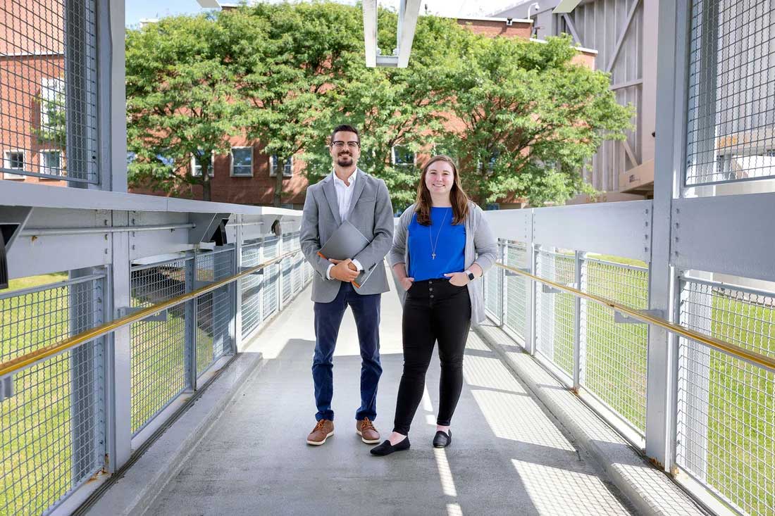 Professor and student stand posed on a bridge on campus