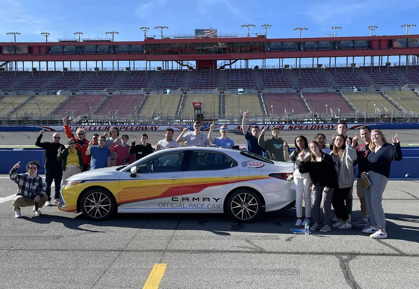 A large group is posed with a NASCAR pace car on a track