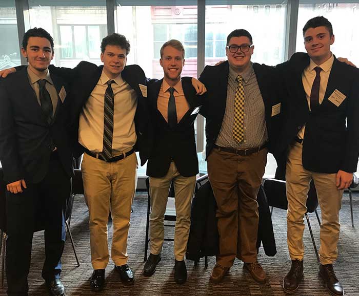 5 male students pose in front of a window in a hall