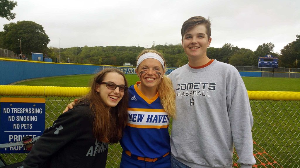 Three young people are posed next to a sports field