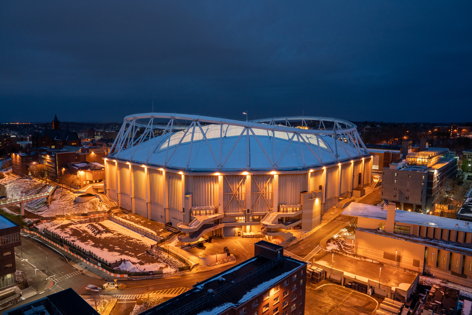 A nighttime photo of the stadium at Syracuse University with the City of Syracuse skyline in the background.