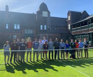 Seventeen people are posed behind a tennis net