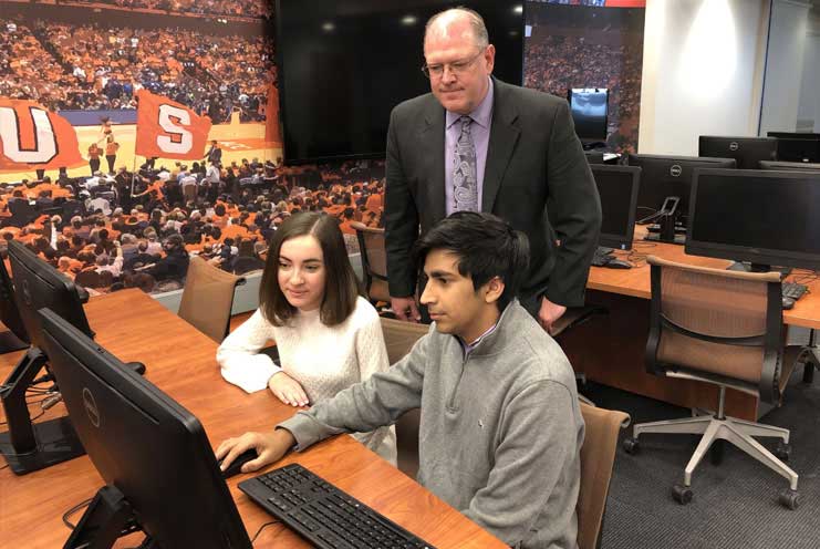 Two students sit at a computer with a professor