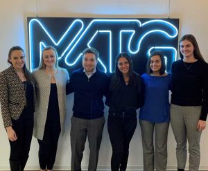 6 students are posed in front of a lit MKTG logo