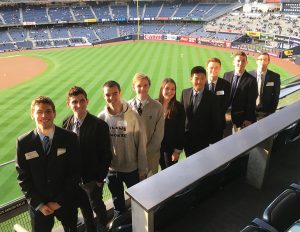 9 students are posed overlooking Yankee stadium field below