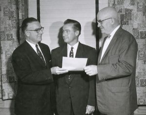 Three men are posed two holding a letter