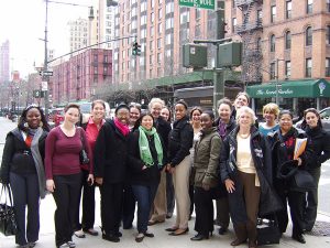 17 persons are posed on a street corner in New York City