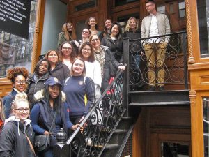 16 persons are posed on a stairwell in the entrance to the Tenement museum in New York City