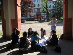 A group of 8 students study in a circle in an outside covered patio