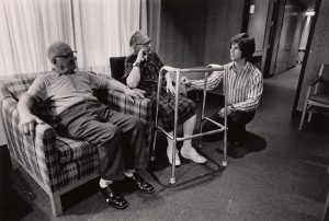 A student kneels and talks with a seated elderly couple