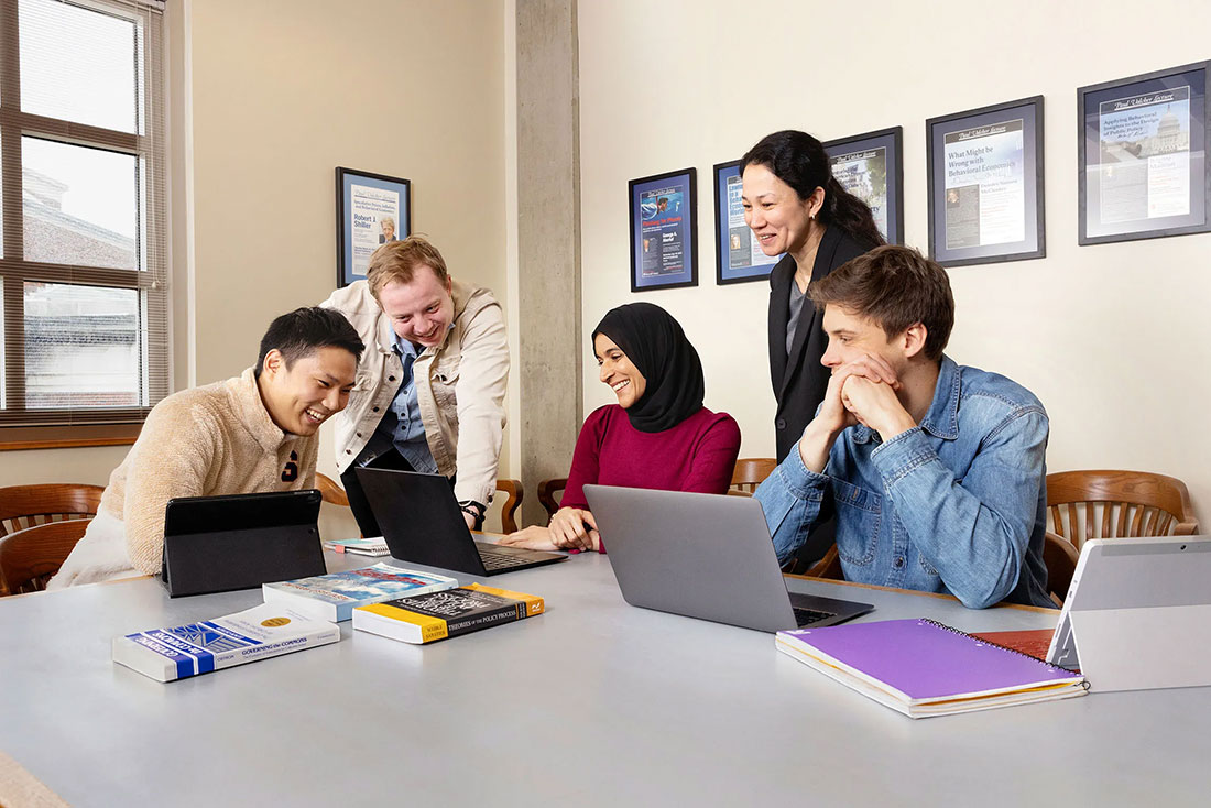 Professor sitting around a table with 4 students look at her computer screen