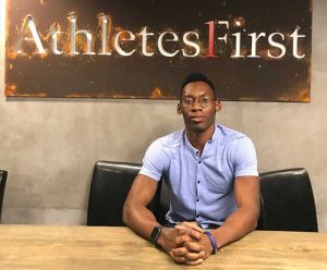 Sean Onwualu sits in front of a sign saying Athletes First