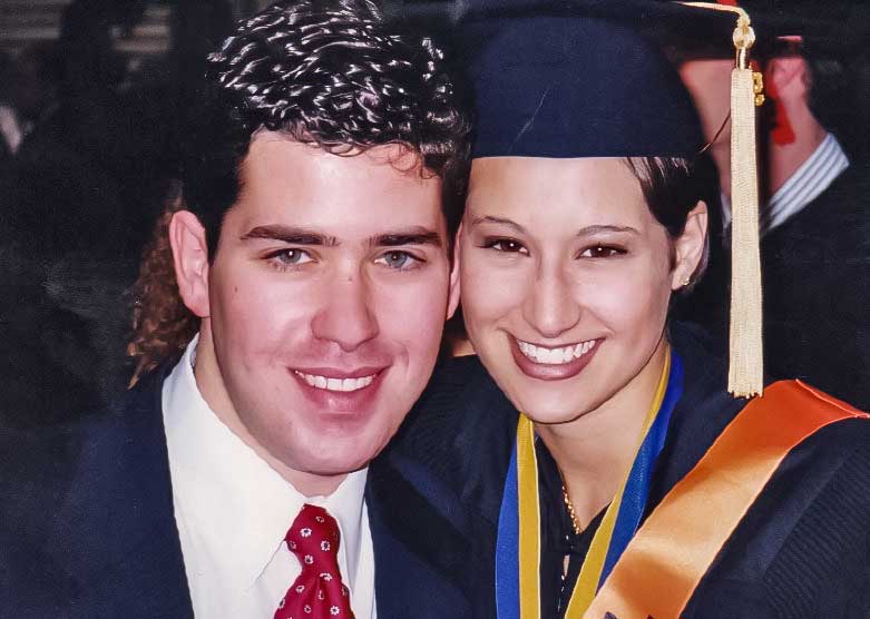 A couple is posed closely together in graduation clothing