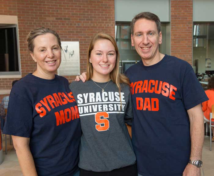A student poses with her parents all are wearing Syracuse University shirts