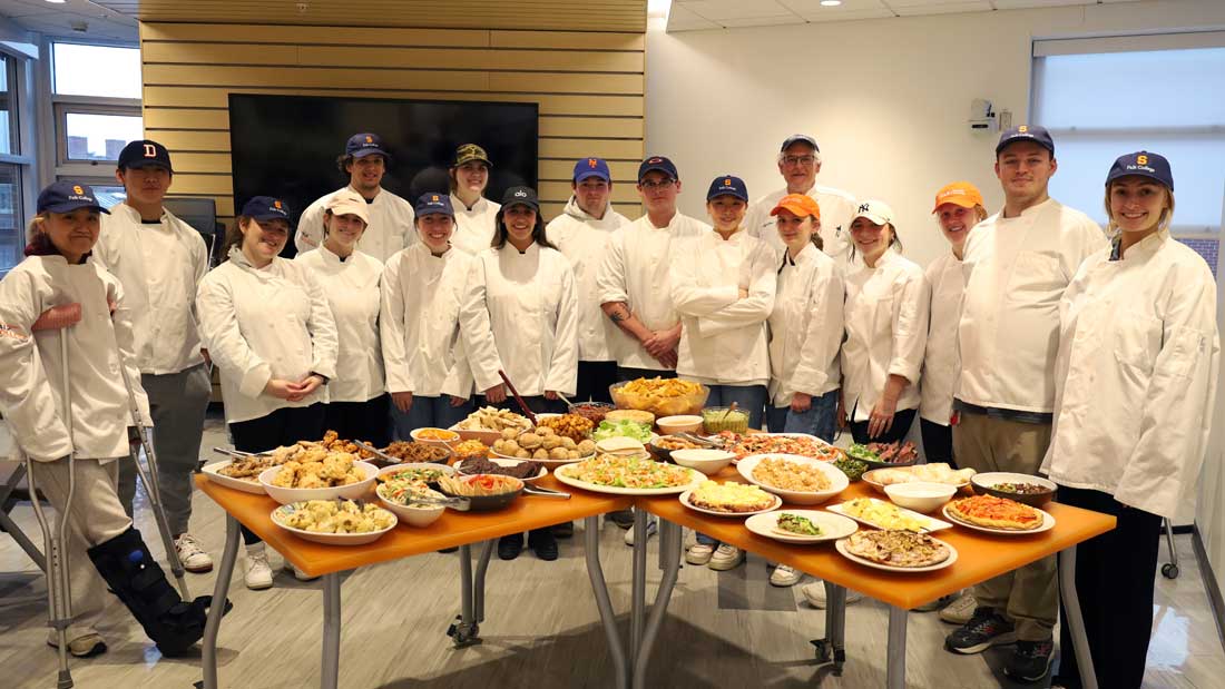 Many people in chef outfits stand around tables full of food