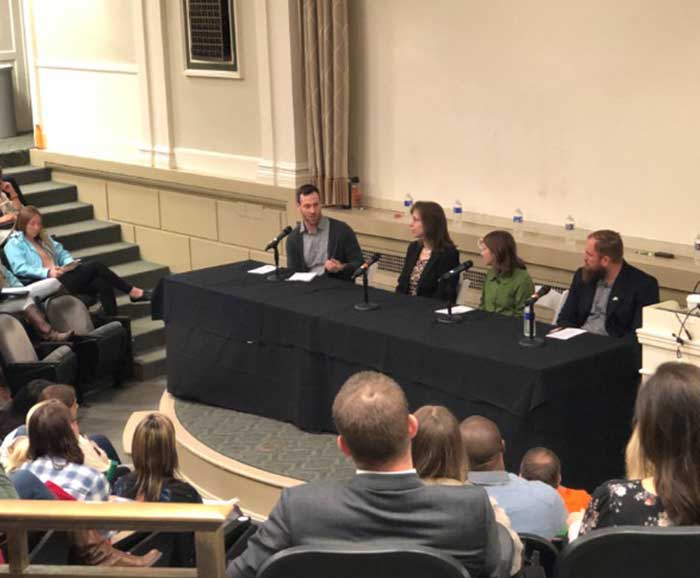 A panel of 4 persons present to an auditorium of people