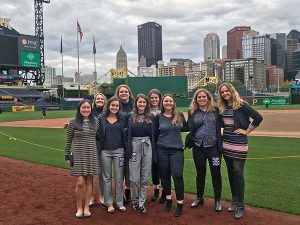 9 young women pose together on a baseball diamond