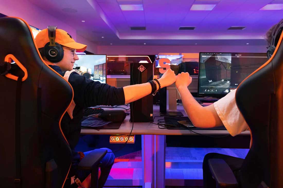 Two students sitting at computers in the eSports room bump fists.