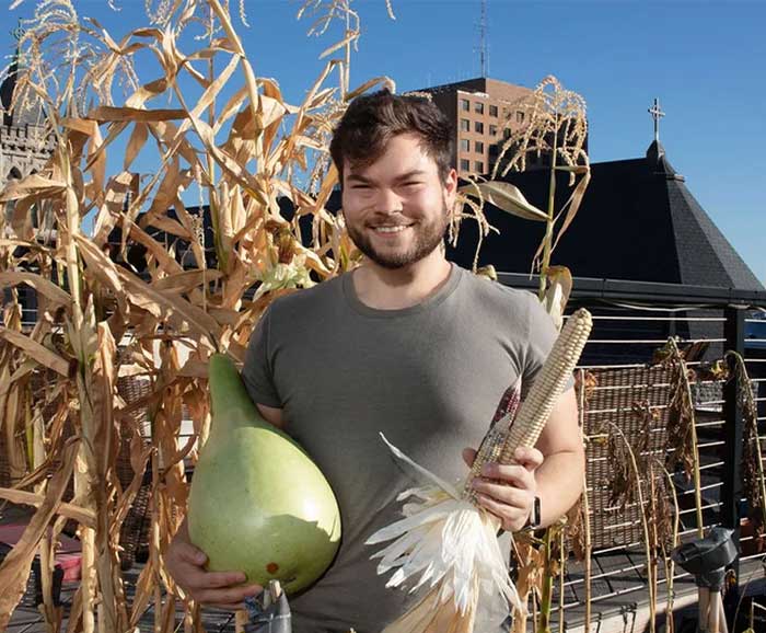 Ethan Tyo stands with vegetables on a rooftop garden