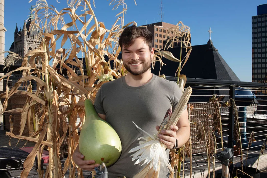 Ethan Tyo stands with vegetables on a rooftop garden