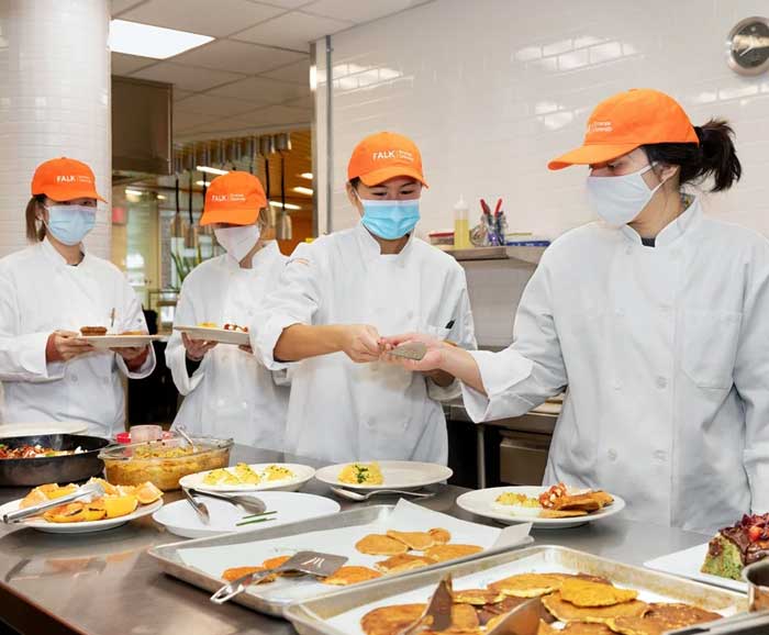 four students are in a commercial kitchen with prepared food