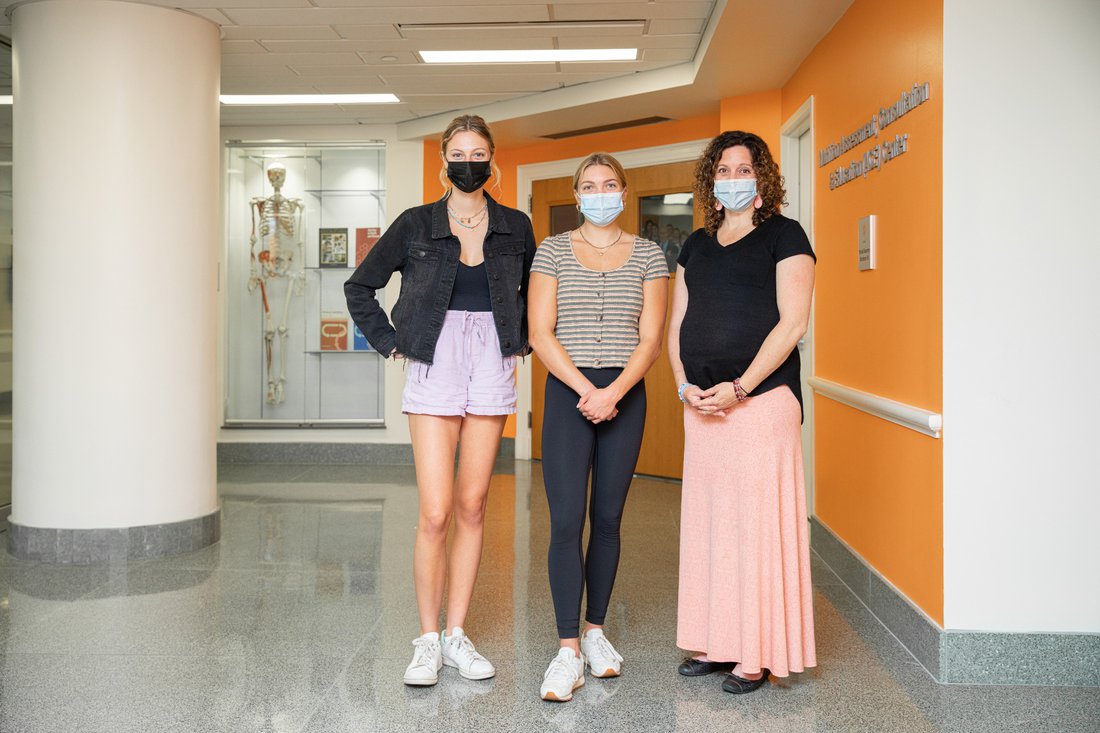 Portrait of two students and professor standing in a building's hallway.