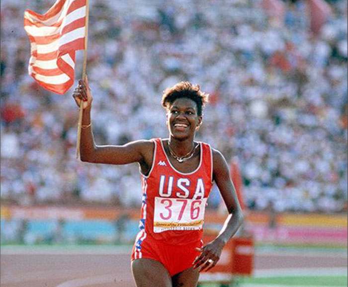 Olympic gold medalist Benita Fitzgerald Mosley on the track carrying the USA flag and smiling