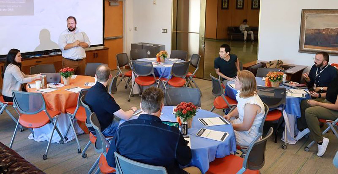 Professor addressing a room of people sitting at round tables