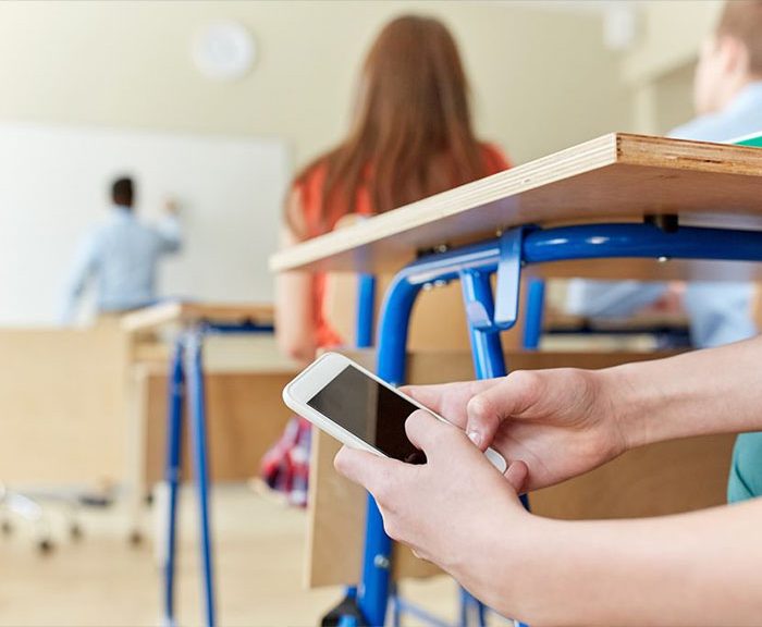 student in classroom on his cell phone which he is hiding under his desk
