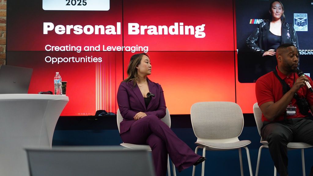 Two people on front of room as presenters with big screen behind them