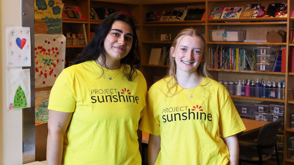 two students stand side by side wearing yellow shirts that say Project Sunshine