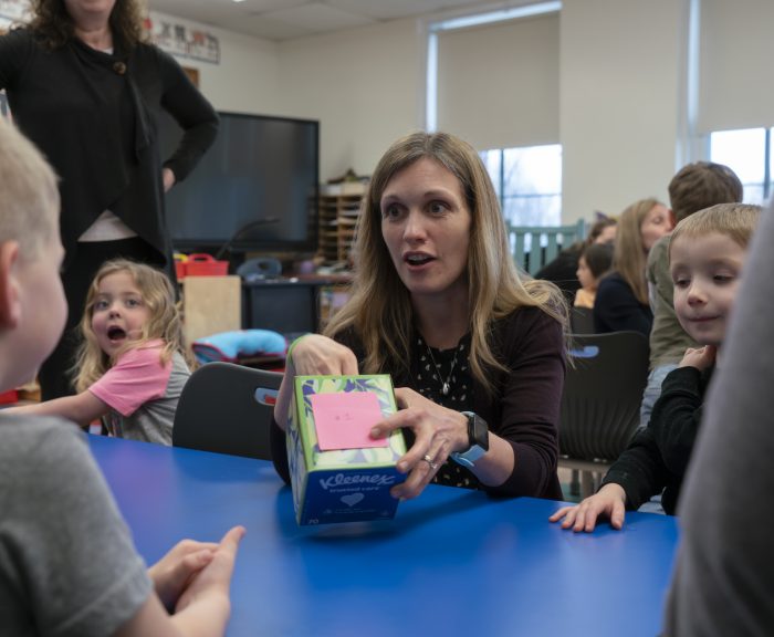 teacher sitting at table with pre-k students