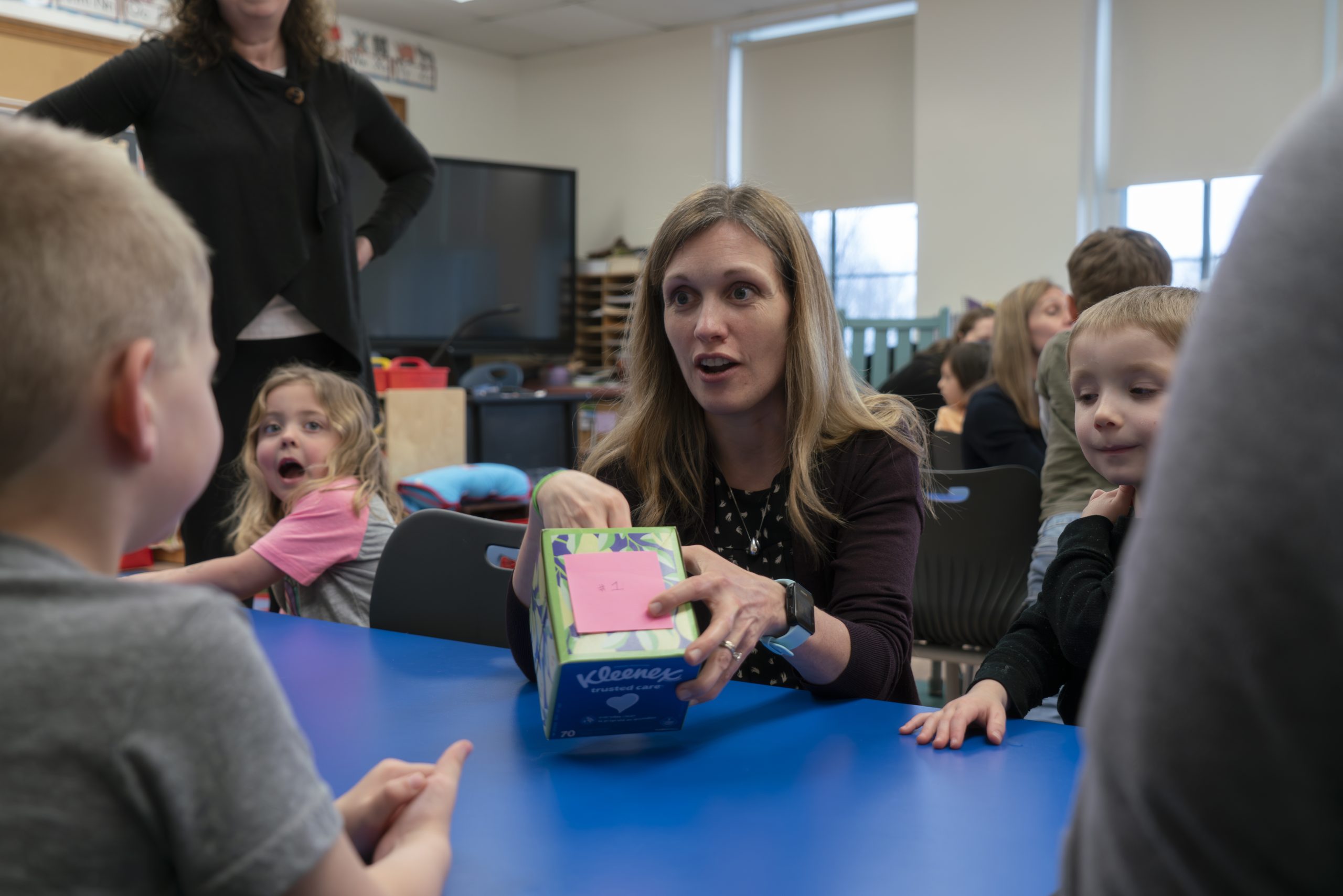 teacher sitting at table with pre-k students
